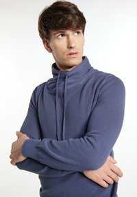 Strukturierter blauer Hoodie mit hohem Kragen, Kordelzugverschluss und langen Ärmeln, der ein geripptes Muster und eine lockere Passform aufweist.