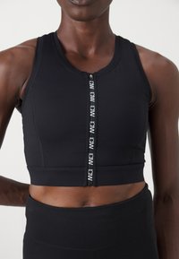 Top desportivo preto com fecho frontal em zip e detalhes de logotipo. Feito de tecido elástico, possui um design ajustado e uma textura suave.
