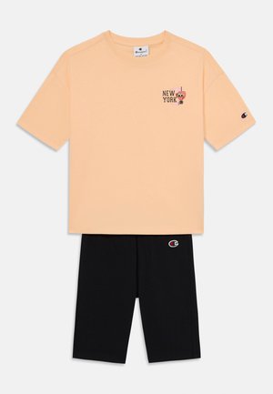 Persika puuvillane T-särk, millel on 'NEW YORK' graafika, ja mustad lühikesed püksid, millel on logo detail. T-särk on lühikeste varrukatega ja ümmarguse kaelusega.