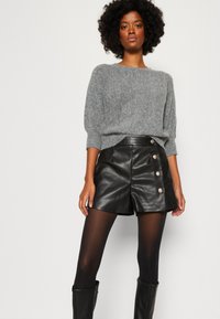 Pull en tricot gris avec une coupe ample, associé à un short en cuir noir taille haute avec des boutons décoratifs et une texture lisse.