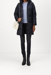 Laivastonsininen toppatakki hupulla, vaaleansininen paita, mustat farkut ja mustat nilkkurit. Valkoinen olkalaukku hopeaketjuhihnalla.