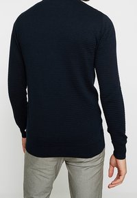 Mörkblå ribbad tröja med lång ärm och rund halsringning. Tillverkad av ett texturerat stickat material, med en figurnära design.