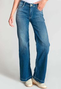 Jeans a gamba larga in denim blu con lavaggio chiaro, dotati di cinque tasche, chiusura con bottone e leggere sfumature per un effetto testurizzato.