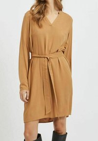 Robe à manches longues et encolure en V de couleur beige chaud avec une ceinture à la taille. Confectionnée dans un tissu lisse et léger avec une coupe décontractée.