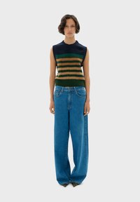 Sleeveless knitted top in dark blue, green, and brown stripes. Paired with loose, high-waisted light blue denim jeans with a relaxed fit.