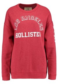 Sudadera de forro polar roja con cuello redondo, que presenta "Los Ángeles" y "Hollister" impresos en blanco, con puños y dobladillo acanalados.