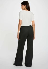 Camicia bianca a maniche corte abbinata a pantaloni a gamba larga grigio antracite a vita alta. I pantaloni hanno una parte anteriore liscia e dettagli con tasche.