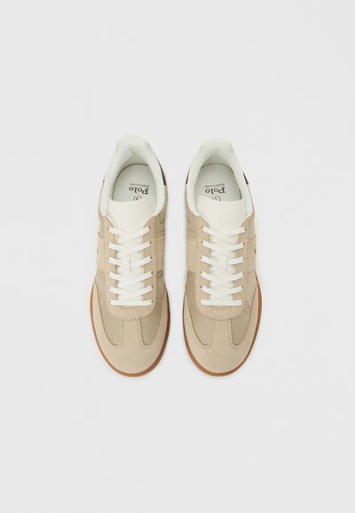 Μπεζ και λευκά αθλητικά παπούτσια καθημερινής χρήσης με λευκά κορδόνια και λαστιχένιες σόλες σε χρώμα καραμέλας, σε φωτεινό γκρι φόντο, φαίνονται από ψηλά.