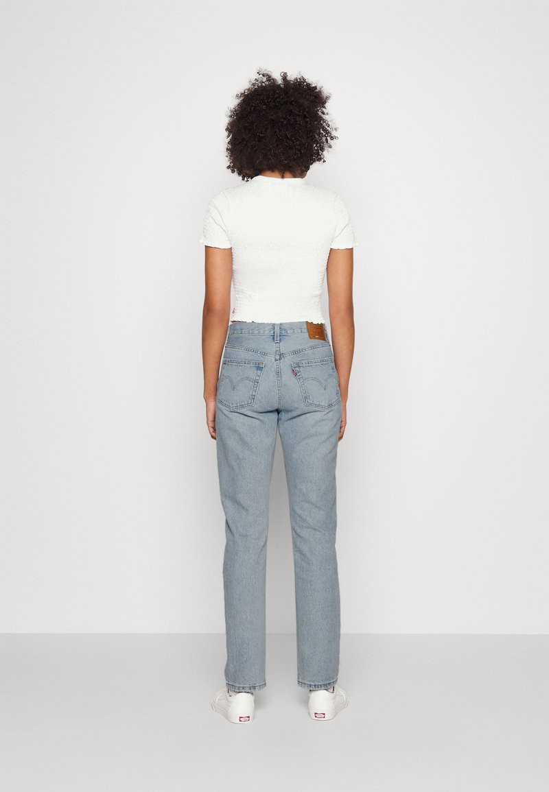 Jeans de mezclilla azul claro con corte recto y bolsillos traseros con detalles de costura, combinados con una blusa corta de manga corta texturizada blanca.