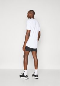 Hvid kortærmet t-shirt parret med sorte sportsshorts, båret med sorte sneakers og hvide sokker. Glat stof med en afslappet pasform.