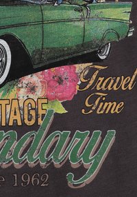 Gráfico de coche vintage verde sobre tela negra, con acentos florales en rosa y amarillo y texto estilizado que dice "Viaje Legendario 1962".