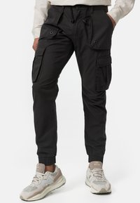 Pantalones cargo negros con puños elásticos, múltiples bolsillos laterales y cintura con cordón. La tela tiene una textura sutil y un tacto ligero.
