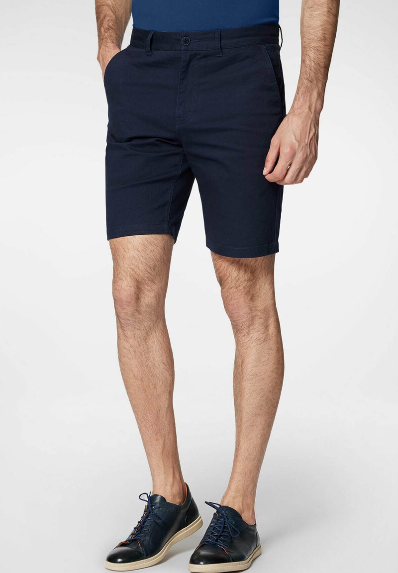 Granatowe szorty z bawełny z zapięciem na guzik, bocznymi kieszeniami oraz dopasowanym krojem, sięgające powyżej kolana na męskim modelu.