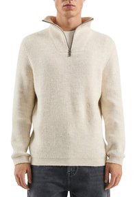 Roomkleurige fleece trui met een halve ritssluiting bij de kraag, met een geribbelde structuur en een losse pasvorm. Lange mouwen met aansluitende boorden.