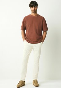 Camiseta de manga corta de color óxido, corte relajado, combinada con pantalones de color crema. Zapatos de ante marrón completan el look.