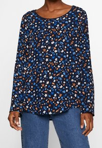 Blusa a maniche lunghe blu navy con motivo floreale in blu, arancione e bianco. Caratterizzata da un collo rotondo e una silhouette rilassata.