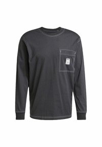 Svart långärmad skjorta med vertikala vita nålrandiga ränder, stickat tyg, rund halsringning, ficka på vänster bröst med logotypmärke, muddade ärmslut.