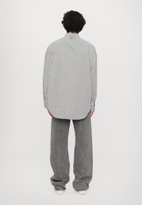 Chemise à manches longues rayée en noir et blanc avec une coupe décontractée. Tissu doux, ourlet arrondi et détails de boutons aux poignets, accompagnée d'un pantalon large gris.