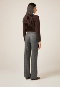 Brown knitted sweater and gray plaid high-waisted trousers. The fabric appears soft, with a loose fit and wide-leg cut. Flat black shoes.