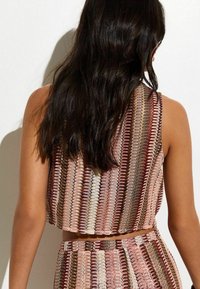 Top corto tejido con un patrón multicolor en tonos de rosa, marrón y crema, con textura acanalada y diseño de espalda descubierta.
