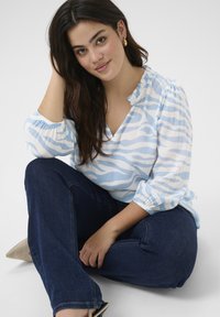 Light blue and white patterned blouse with puff sleeves, V-neck, paired with dark denim jeans. Smooth texture and casual fit.