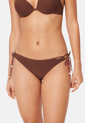 Mujer con bikini marrón texturizado con braguitas atadas al lado que muestran pequeños detalles de cuentas en los cordones, vista desde la mitad del pecho hasta la parte superior de los muslos.