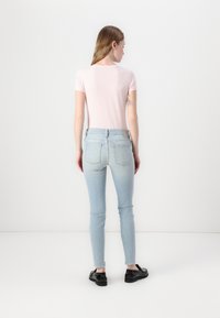 Camiseta ajustada de color rosa claro con mangas cortas, combinada con jeans skinny de talle alto en un azul claro y zapatos negros, vista desde la parte posterior.
