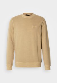 Sweatshirt bege de gola redonda feito de material suave, com punhos e barra canelados, apresentando uma pequena etiqueta tonal com logo no peito.