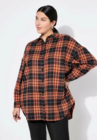 Camicia a quadri arancione e nera con chiusura a bottoni, taglio oversize e maniche lunghe, realizzata in un tessuto morbido con orlo rilassato.