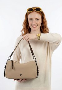 Punapäine naine kollaste päikeseprillidega hoiab käes beežikas käekotti, mille rihm on leopardimustriline, ta kannab beežikat kampsunit ja kuldset kella.