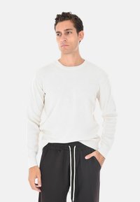 Maglione bianco a maniche lunghe con righe, colletto rotondo, abbinato a pantaloni neri con cordoncino. La texture è liscia e progettata per una vestibilità rilassata.