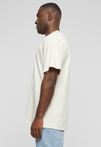 Kortermet T-skjorte med rund hals i off-white bomull. Løs passform med subtil tekstur. Kombinert med lyseblå denimjeans.