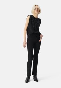 Top senza maniche nero con cuciture geometriche argentate, abbinato a jeans neri a vita alta e stivali alla caviglia. Design minimalista.