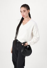White, knitted v-neck sweater with long sleeves, paired with black high-waisted jeans. The model holds a small, black, leather handbag.