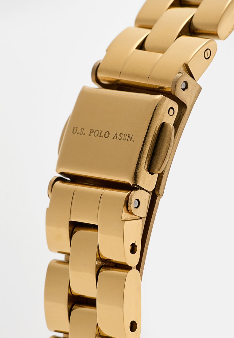 Goldener Metall-Uhrenarmband mit polierten Gliedern, ausgestattet mit einem Verschluss, der mit "U.S. POLO ASSN." graviert ist. Präsentiert eine elegante, glatte Textur.