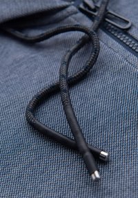 Cordons tressés noirs et gris sur un fond de tissu texturé bleu, avec des embouts en métal arrondis et une finition lisse.