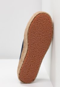 Espadrilová podrážka s textura hnědé gumy, obklopená pleteným jutem. Svršek je z tmavě modré látky.