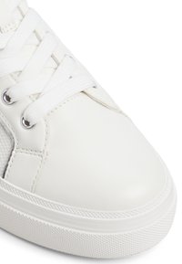 Zapatillas blancas con una parte superior sintética suave, cordones blancos planos y una suela de goma texturizada. Los paneles laterales incluyen un detalle de malla.
