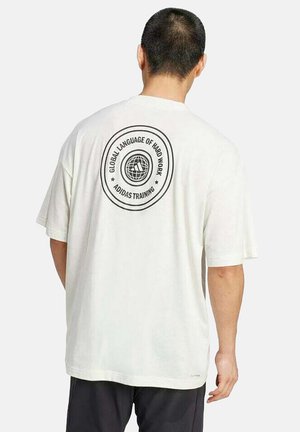 Man in een wit Adidas T-shirt met het logo "Global Language of Hard Work Adidas Training" en een wereldbolafbeelding op de achterkant.