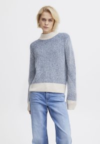 Sweter z dzianiny z wysokim kołnierzem, w niebiesko-białe pionowe paski. Miękka faktura, żebrowany design oraz kontrastowe wykończenia mankietów i dolnej części.