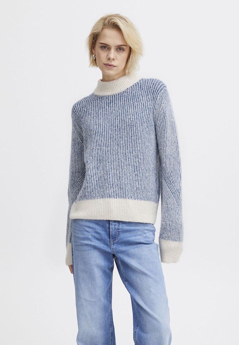 Sweter z dzianiny z wysokim kołnierzem, w niebiesko-białe pionowe paski. Miękka faktura, żebrowany design oraz kontrastowe wykończenia mankietów i dolnej części.