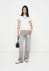 T-shirt blanc ajusté avec broderie florale rouge, associé à un jean large gris clair. Accessoirisé avec un petit sac à main bleu marine et des chaussures crème.