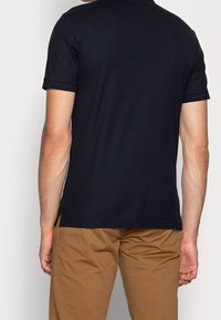 Czarna koszulka polo z krótkim rękawem, wykonana z bawełny, z prostym dołem i bocznymi rozcięciami, w połączeniu z khaki spodniami. Teksturowana tkanina.