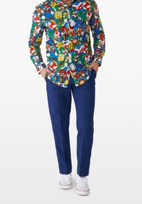 Camicia colorata con bottoni, decorata con una stampa di personaggi di videogiochi in vari colori; abbinata a pantaloni blu scuro e sneakers bianche.