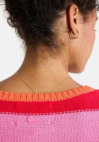 Rücken und Nacken einer Frau mit lockigem, hochgestecktem Haar, die goldene Creolen trägt, eine zarte goldene Halskette und einen pink-roten Strickpullover.