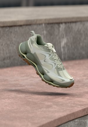 Light green athletic shoe with thick cushioned sole and mesh details, floating above stone steps in outdoor setting.