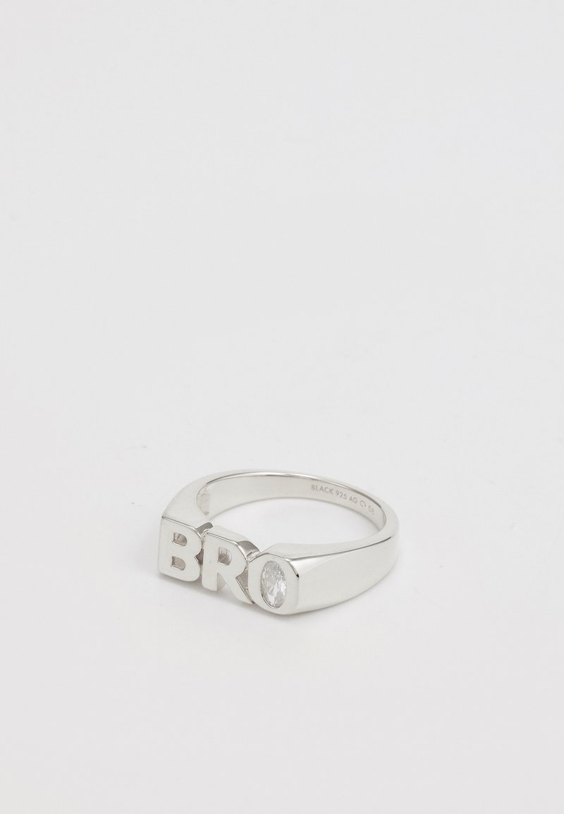 Anillo de plata con las letras "BRO" en un diseño en negrita, con una textura suave y un acento de piedra preciosa clara y redonda en un lado.