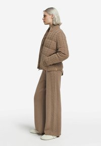 Beige vadderad jacka med hög krage och sidofickor, kombinerad med vida stickade byxor med flätmönster. Vita skor.