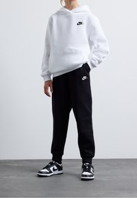Vit huva sweatshirt med en svart Nike-logga, parat med svarta sweatpants med en matchande logga, och svartvita sneakers.