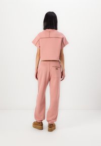 Rosa, kastige Strickjacke mit rundem Ausschnitt, kurzen Ärmeln und Stichdetails, kombiniert mit passenden rosa Jogginghosen und braunen Plateau-Schuhen.